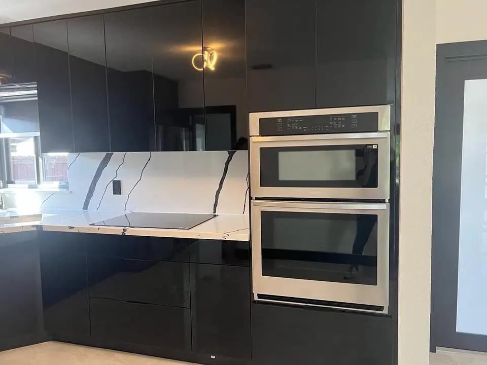 Glossy black kitchen with marble-look backsplash and built-in wall ovens