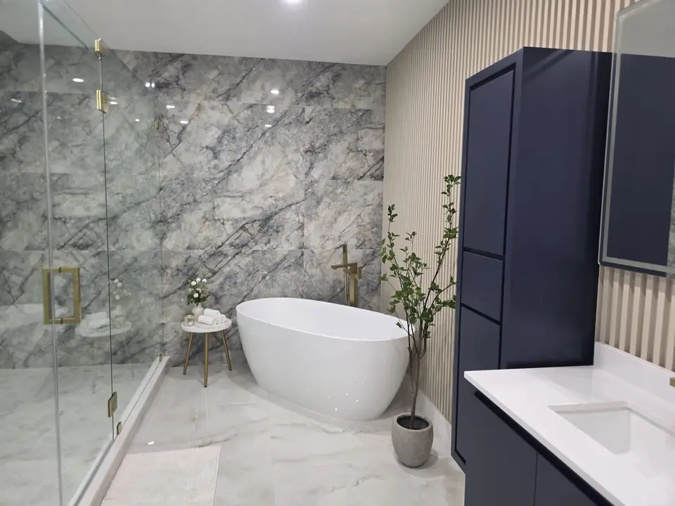 Bathroom with gray marble-look feature wall, freestanding tub and navy linen tower