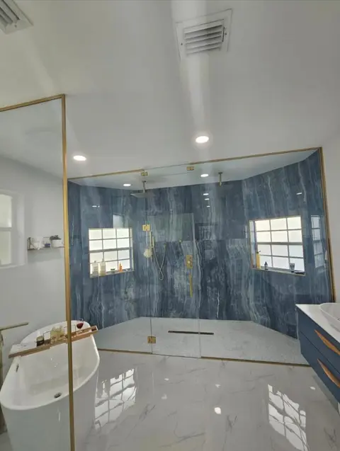 Brass-framed glass shower with blue-gray stone-look walls and dual shower heads